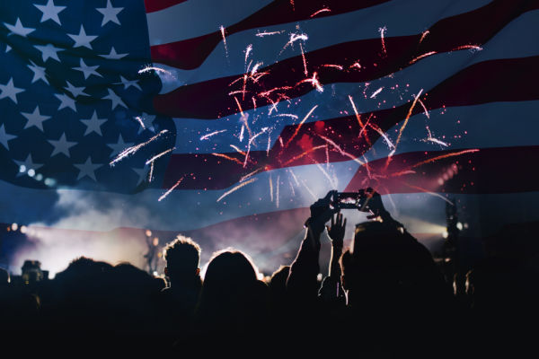 American flag superimposed over fireworks above a crowd.