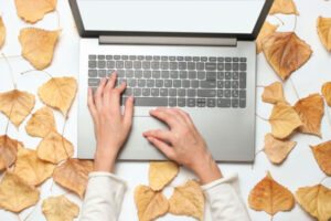 A woman's hands on a laptop keyboard, surrounded by autumn leaves