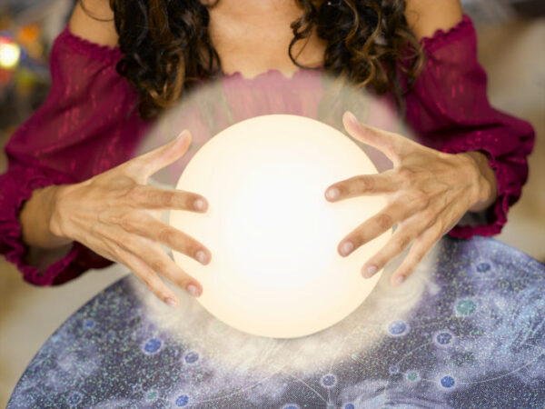 a fortune teller woman's hands touch a glowing ball on a table