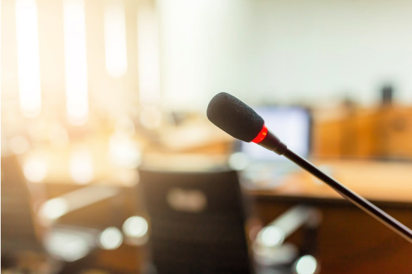 a microphone in focus, with a board room, table and chairs for an audience in the background.