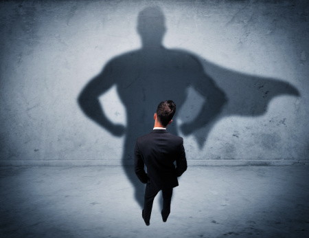 A man in a business suit looks at a wall where his shadow is wearing a superman-type cape. boost your confidence and polish at work