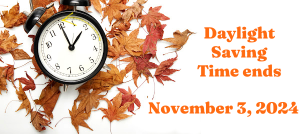 An alarm clock lies on a bed of red and brown autumn leaves. A yellow arrow on the clock curves to the left, indicating moving the clock backward. Text reads Daylight Saving Time ends November 3, 2024.