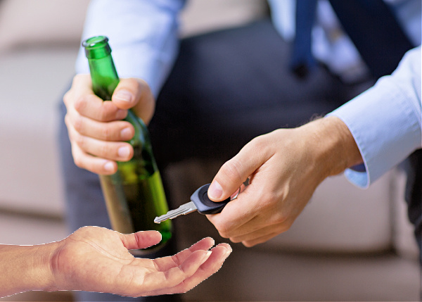 A hand reaches out to take car keys away from a man in a suit who is holding a beer.