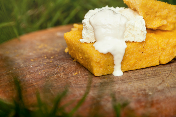 A slice of corn pudding topped with cream rests on a primitive wooden plate.