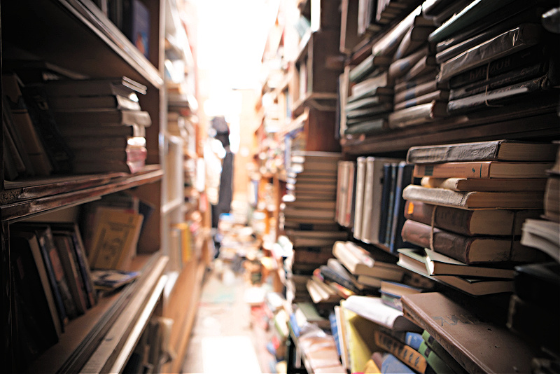 An overstuffed library aisle with reference books shelved haphazardly and loose papers on the shelves.